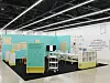 Museum exhibition space with turquoise panels, display tables, and informational wall text.