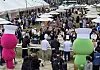 Crowds browse bakery stalls at an outdoor bread festival with colorful mascot figures in the foreground.