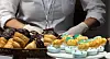 Trays of assorted pastries and decorated desserts displayed at a bakery fair.