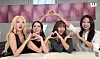 Four women posing together and making hand heart gestures in front of a pink backdrop.