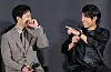 Two actors smile and gesture while holding microphones at a film briefing event.