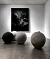 Three large textured spheres displayed in a gallery beneath a black-and-white abstract wall piece.