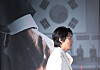 Actor stands in profile at a film production briefing with a large movie poster in the background.
