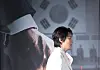 Actor stands in profile at a film production briefing with a large movie poster in the background.