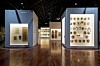 Two glowing exhibition cases with artwork and objects in a museum gallery with polished wooden floors.