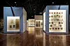 Two glowing exhibition cases with artwork and objects in a museum gallery with polished wooden floors.