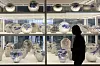 Silhouette of a visitor in front of shelves of blue-and-white ceramic pottery at a museum exhibition.