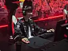 Esports player in a black team jacket gaming at a computer in a red-lit arena.