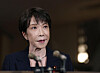 Japan's Prime Minister Sanae Takaichi speaks into microphones in a dimly lit Tokyo residence.