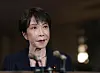Japan's Prime Minister Sanae Takaichi speaks into microphones in a dimly lit Tokyo residence.