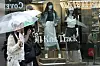 Shop window displaying fall knitwear and mannequins as pedestrians with umbrellas pass outside.