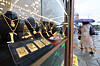 Gold bars and necklaces displayed behind glass at a Seoul gold exchange, with pedestrians visible outside.