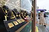Gold bars and necklaces displayed behind glass at a Seoul gold exchange, with pedestrians visible outside.