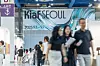 People walk through an indoor venue beneath a large Kia Seoul banner.
