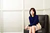 Woman in a navy sweater seated in a dark armchair beside a white paneled wall.