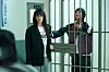 Two people stand on opposite sides of metal bars inside an institutional building.
