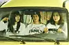 Three passengers in matching FAMILY shirts sit inside a yellow car.