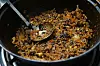 Browned food mixture with a metal spoon in a black frying pan