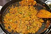 Orange-seasoned rice with green herbs fills a large pan beside a wooden spatula.