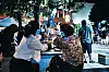 People sit together at an outdoor table under trees during a lively evening street gathering.