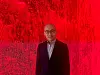 Man in glasses and a dark suit posed against a bright red textured backdrop.