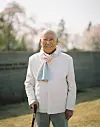 Smiling elderly man in glasses holding a cane outdoors in a garden setting.