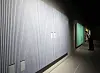 A visitor examines art beside a large vertically textured white installation in a dim museum gallery.