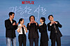 Five cast members and director pose beneath a Netflix logo at a film presentation in Seoul.