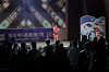 Performer in red on a lit stage before a silhouetted audience, with colorful graphics at right.