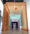 Modern glass corridor framed in orange with teal panels and distant doorways.