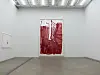 Large red abstract artwork displayed on a white gallery wall beside a smaller framed piece.