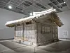 Intricately woven shelter installation displayed in a spacious white gallery.