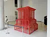 Large red wire sculpture displayed in a bright gallery with visitors nearby.