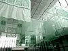 Translucent green patterned panels hang from a high ceiling in an indoor installation.