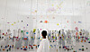 A visitor in white stands before a large colorful suspended installation in a bright museum gallery.