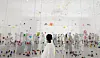 A visitor in white stands before a large colorful suspended installation in a bright museum gallery.