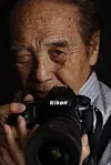 Close-up of a photographer holding a Nikon DSLR camera against a dark background.