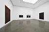 White contemporary gallery with dark artworks on the walls and a polished concrete floor.