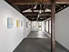 Interior gallery with framed artworks, exposed timber beams, large windows, and a dark polished floor.
