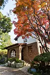 Historic brick house surrounded by colorful autumn trees, shrubs, rocks, and a paved walkway.