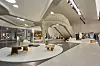 Modern shopping interior with curved columns, seating, display counters, and polished floors.