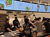 Crowded restaurant counter with customers ordering beneath illuminated menu boards.