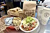 Handcrafted chips, salad, wrapped food, and a takeaway drink on a restaurant table.