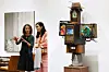 Two visitors stand beside a vintage television sculpture topped with a hat in a white gallery at Frieze Seoul.