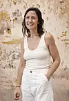 Smiling woman in white clothing standing before a textured floral wall.