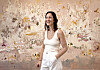 Smiling woman in white clothing standing before a pastel abstract floral painting.