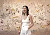 Smiling woman in white clothing standing before a pastel abstract floral painting.