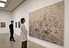 Two visitors look at a large textured abstract painting in a minimalist art gallery.