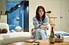 Han So-hee as Seon-woo sits on a sofa in a softly lit room beside a table with drinks.