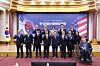 Officials pose beneath a Korea-U.S. banner in a formal hall, with a wheelchair user seated at right.